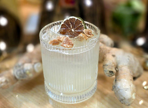 Refreshing cocktail with a lime garnish, ice, and ginger root in background.