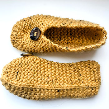 A pair of knit slippers in a mustard yellow yarn against a white background.