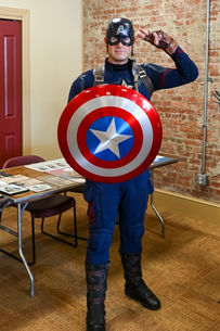 Photo of man dressed as Captain America posing with shield in front of a brick wall