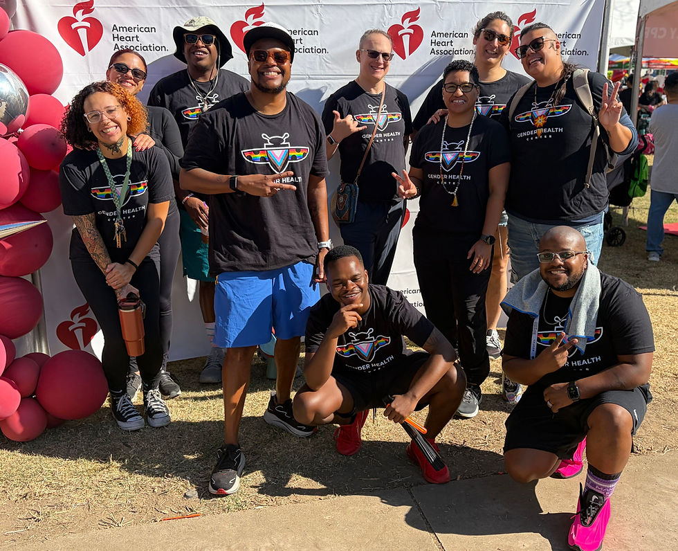 Smiling group in Gender Health Center shirts poses at an American Heart Association booth with pink balloons and a banner backdrop.
