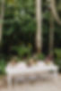 Outdoor celebration space with a sleek white table and crystal-clear chairs, set among natural greenery with decorative lights, perfect for relaxed yet stylish event furniture rentals.