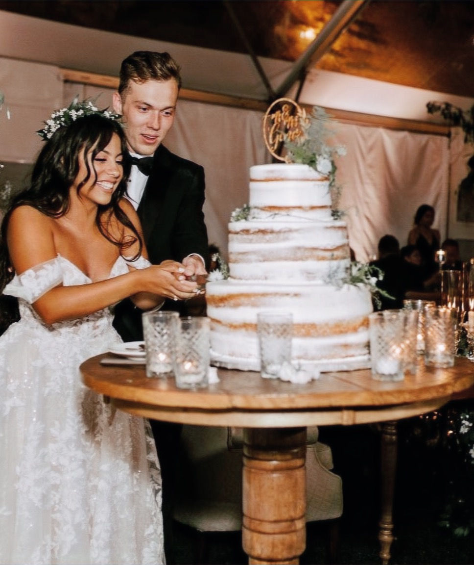 Bride and groom cutting cake on a cocktail table adorned with candles and greenery.
