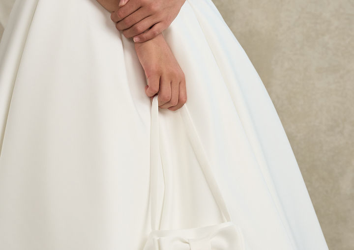 Close-up of the Elva Communion dress with matching satin handbag, showcasing the luxurious heavyweight matte satin fabric and elegant minimalist design.