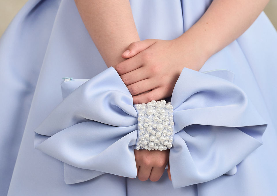 Girl holding the matching satin bow handbag designed to complement Confirmation Dress Clodagh with pearl embellishments.