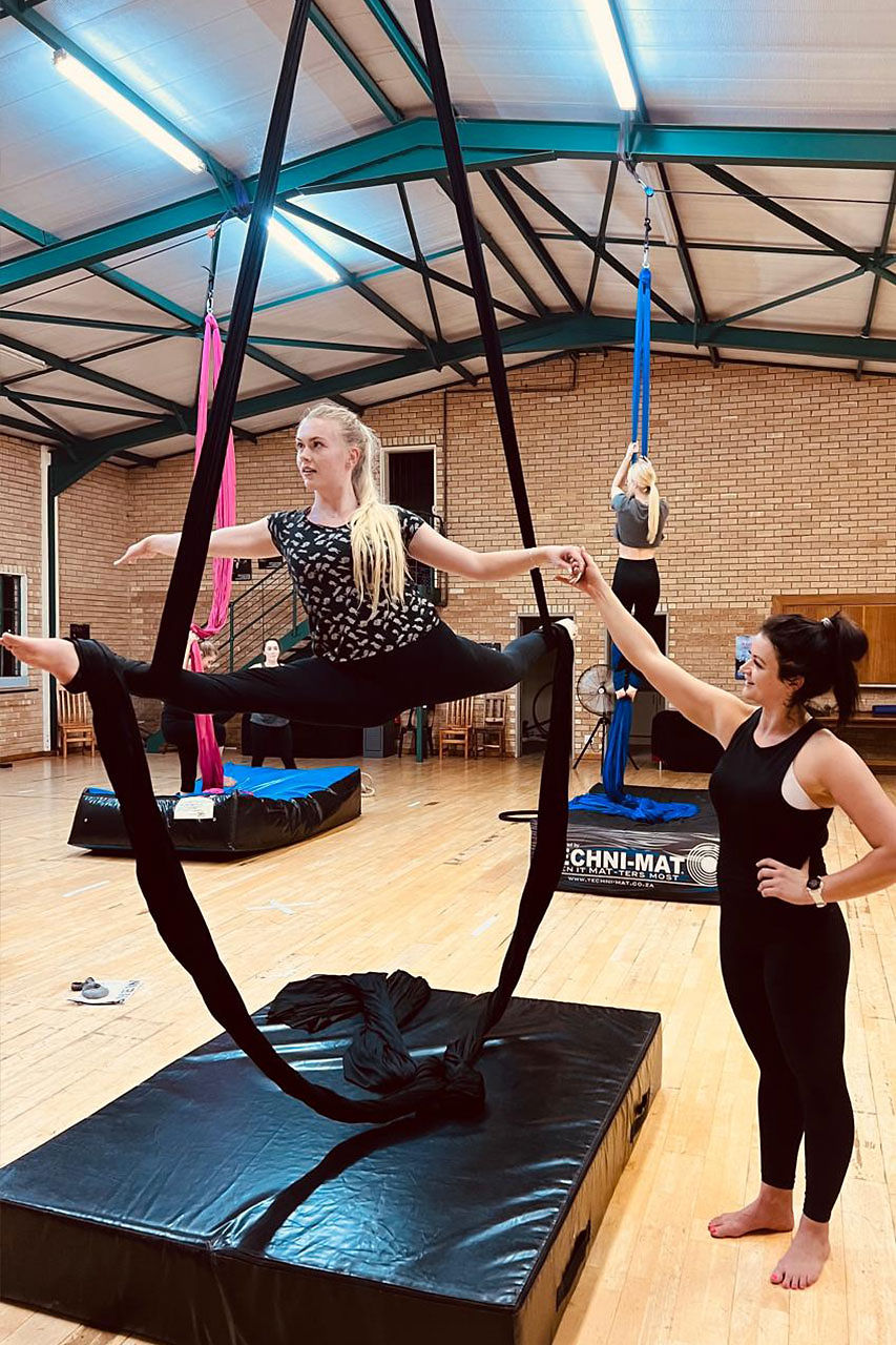 Woman in aerial silks split with instructor during aerial dance class