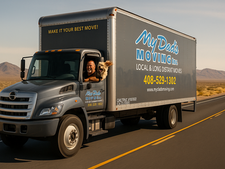 A sleek gray “My Dad’s Moving Inc.” truck cruises along an empty desert highway under a clear sky. Rick Lopez leans out the driver’s window, smiling, while a scruffy dog pokes its head out beside him, its fur blowing in the wind.