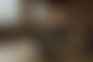 A middle-aged technician wearing a Heavenly Touch Stone Care uniform operates a professional concrete polishing machine on a loft floor. The scene shows half-polished concrete, exposed brick walls, large industrial windows, and a distant city skyline. The lighting highlights the transformation from raw to glossy concrete.