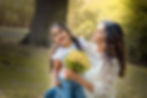 Mother and daughter laughing together while holding a bunch of yellow flowers in a park.