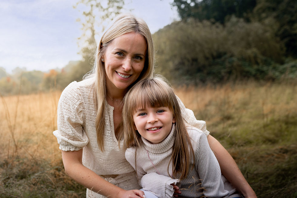 Mother cuddling her daughter whilst sitting together in a grassy field.