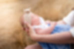 Close-up portrait of a newborn baby wearing a cream bow headband while being cradled in a parent's arms outdoors.
