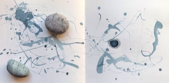Mark-making in a sketchbook using blue acrylic ink pages weighted by 2 pebbles