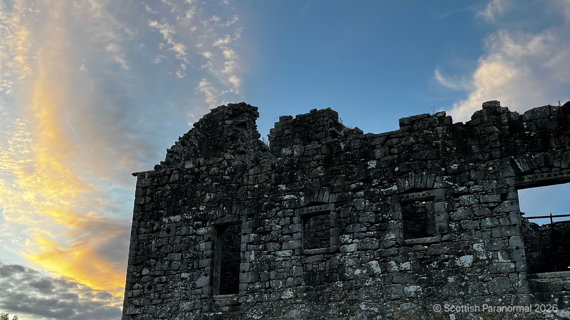 Torwood Castle’s ruined outer wall beneath a gold and blue sunset sky.