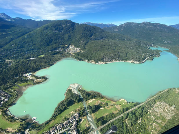 Aerial view of a turquoise lake amidst green mountains.