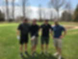 Four men posing on a golf course on a sunny day