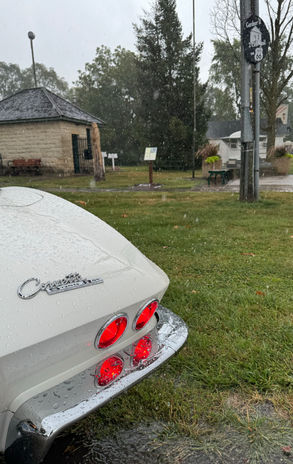 White classic car parked on wet grass near a stone building
