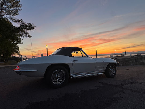 White Corvette convertible parked against a vibrant sunset