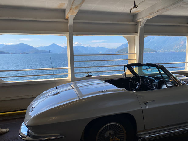 Classic white convertible on ferry, mountains and water view