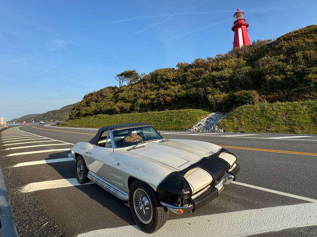 White convertible car parked by a coastal road, red lighthouse