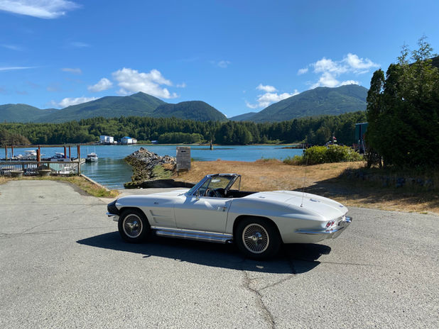 White classic convertible car parked by a bay with mountains