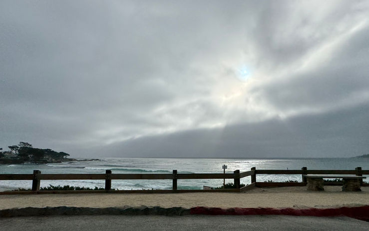 Wooden fence by ocean under cloudy sky