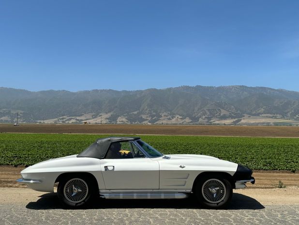 White classic convertible car by field and mountains