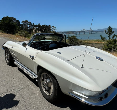 White classic convertible car, water and bridge in background