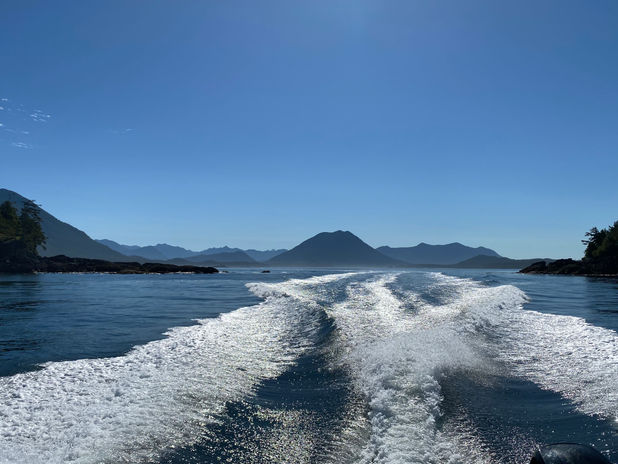 Boat wake on blue ocean receding towards mountains under clear sky