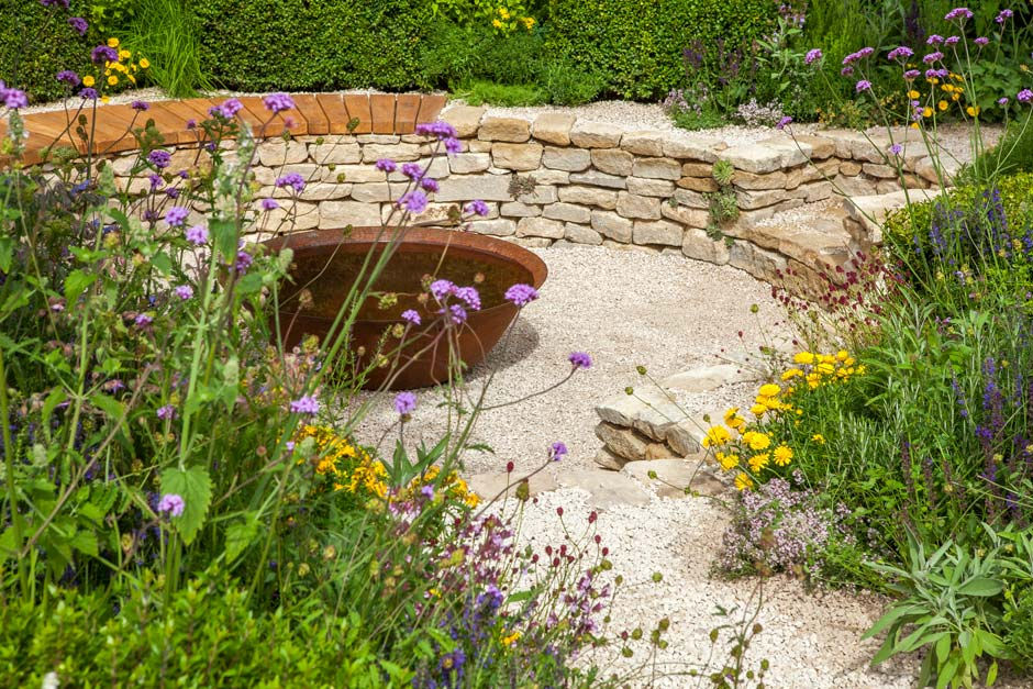 Naturalistic garden design with a curved limestone wall, oak bench seat, corten steel fire bowl and layered mix of perennial and herb planting