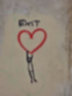 A drawing of drawing of a person holding onto a red heart spray painted on a white wall with the word EXIT painted above.