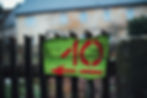 Wooden handcraft house number sign with a green background and red number 10 and red arrow pointing to the left. It's hung on a wooden picket fence.