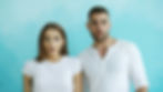 Two white people with surprised expressions stand against a light blue background, both wearing white shirts. The mood is startled.