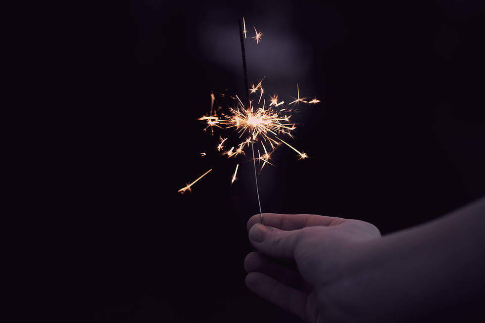 Image of a white hand holding a lit sparkler with a dark background.
