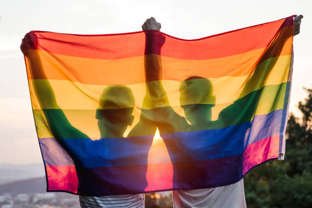 Two people stand arms upraised holding the Rainbow Flag