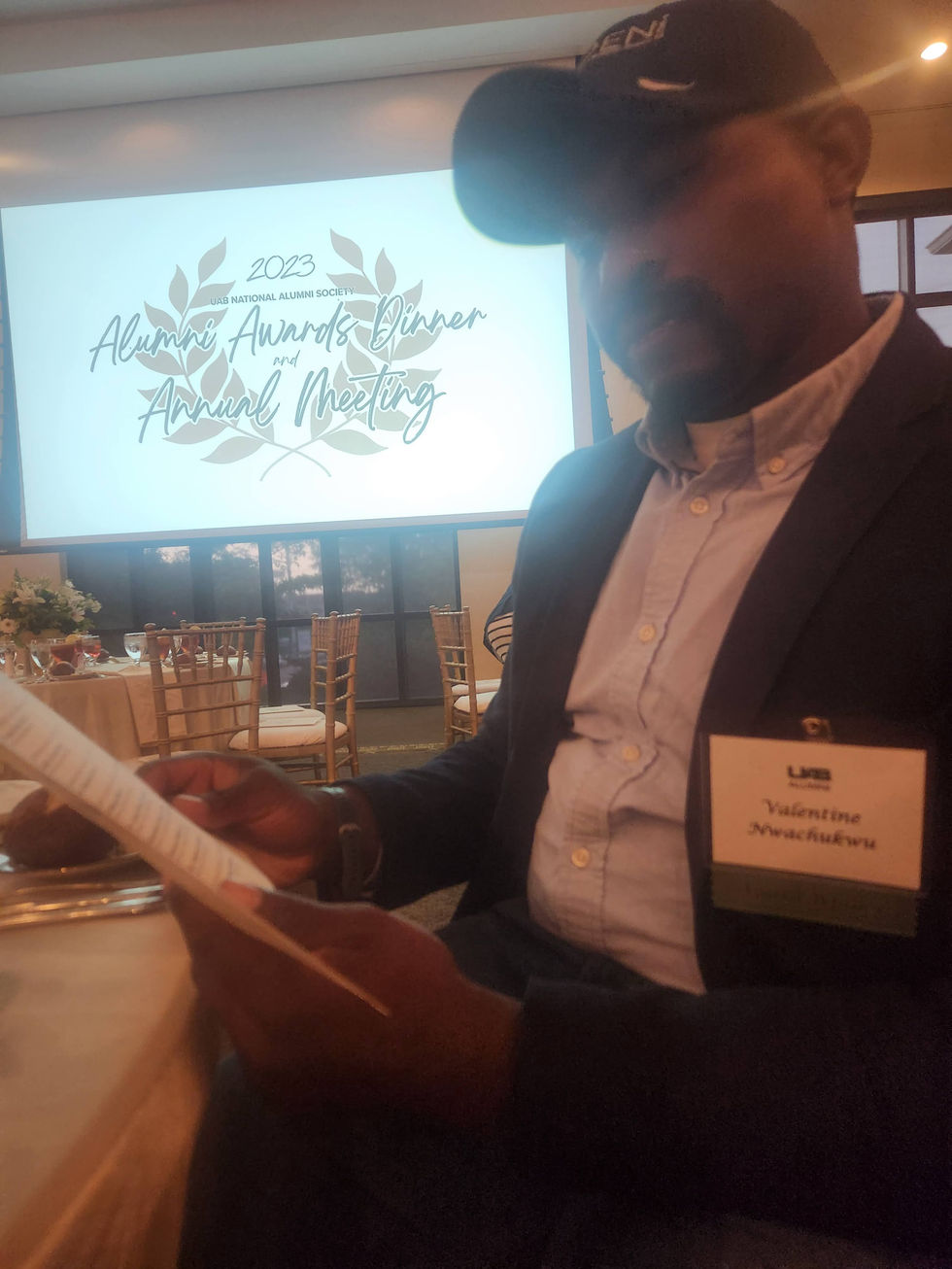 a man sitting in front of a screen that says 2023 alumni awards dinner and annual meeting