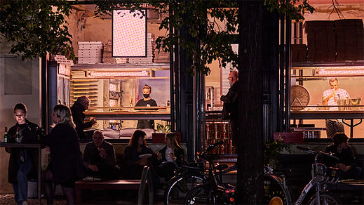 Magic john's from the outside in the evening with people having pizza outside