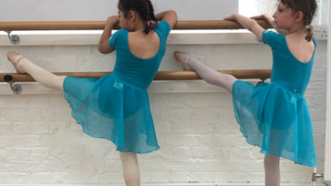 Primary ballet dancers stretching at the barre