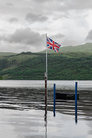 Union Jack flag on a pole with a boat tied up at high tide in sea Loch Sunart at Strontian
