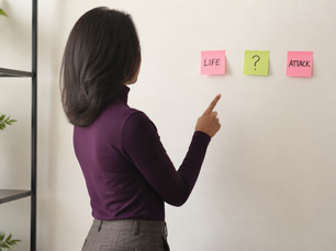 Black woman in plum turtleneck pointing at sticky notes labeled LIFE and ATTACK with question mark between them