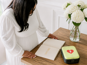 Black woman in white standing over a journal marked DREAMS with an AED machine beside it on a table.