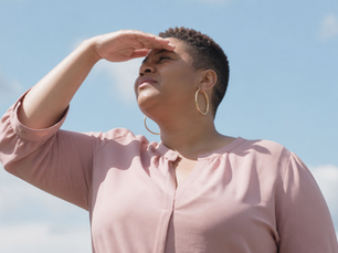 Black woman with a short natural TWA and hoop earrings in blush pink shielding her eyes, looking intently into bright light.