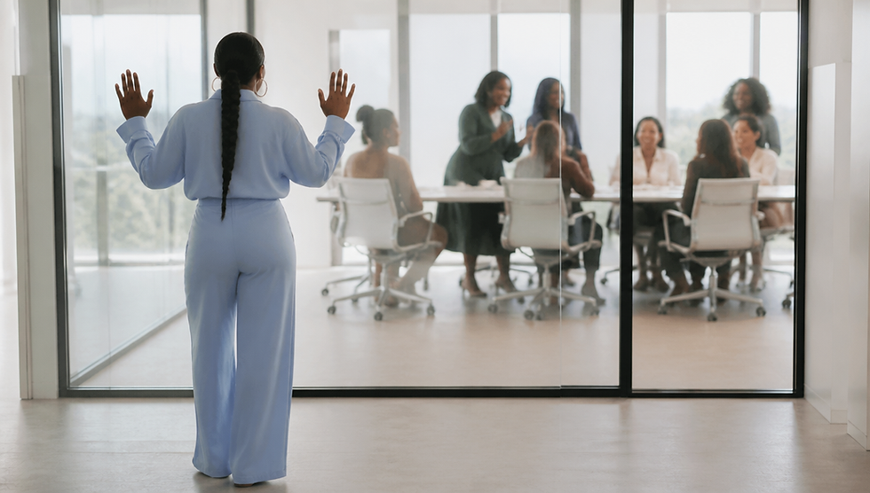 Black woman with braided ponytail in light blue top pressing hands against glass window looking at women in a meeting room inside
