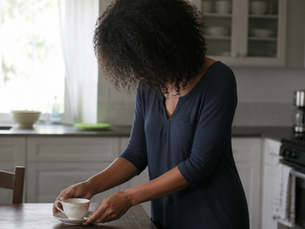 Black woman with a natural afro in navy setting a delicate china teacup on a plain kitchen table on an ordinary day.
