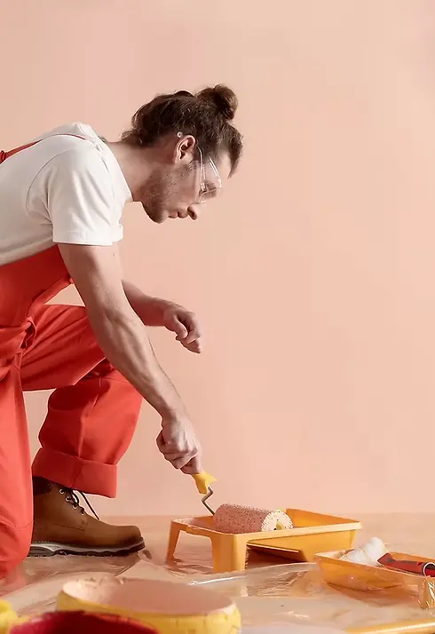 Erkek boyacı turuncu tulumuyla duvarı şeftali rengine boyuyor.