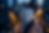 Close-up lifestyle photography of a person holding an iPhone with a dual-camera system against a blurred, golden bokeh city background. The mood is modern and tech-focused in an evening urban setting.