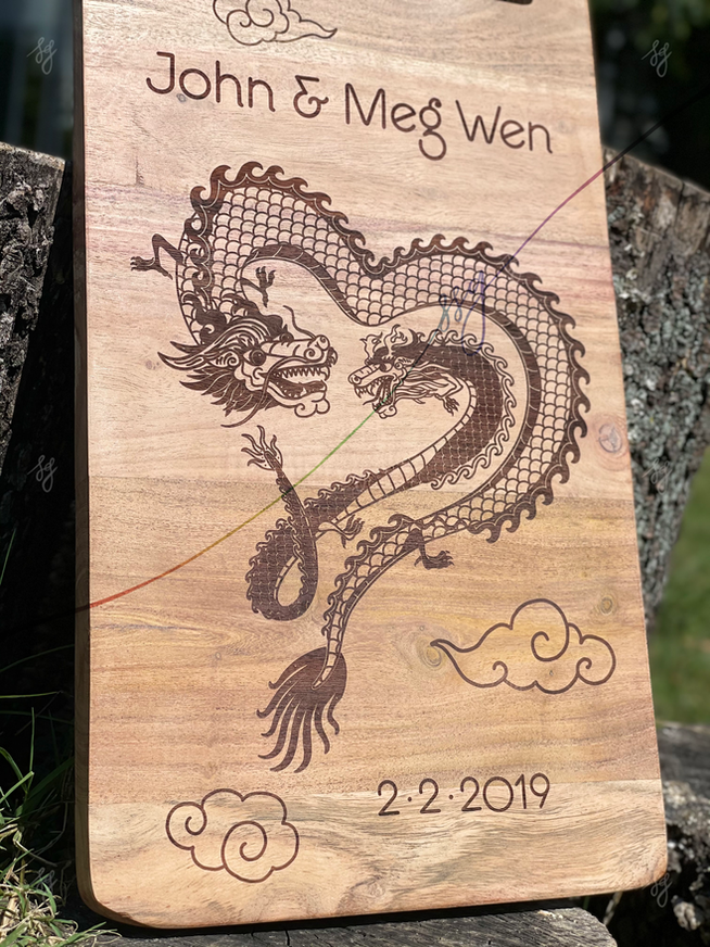 Image: A rectangular wooden cutting board laser-engraved with an illustration of two Chinese zodiac dragons forming the shape of a heart

Text: John & Meg Wen, 2-2-2019