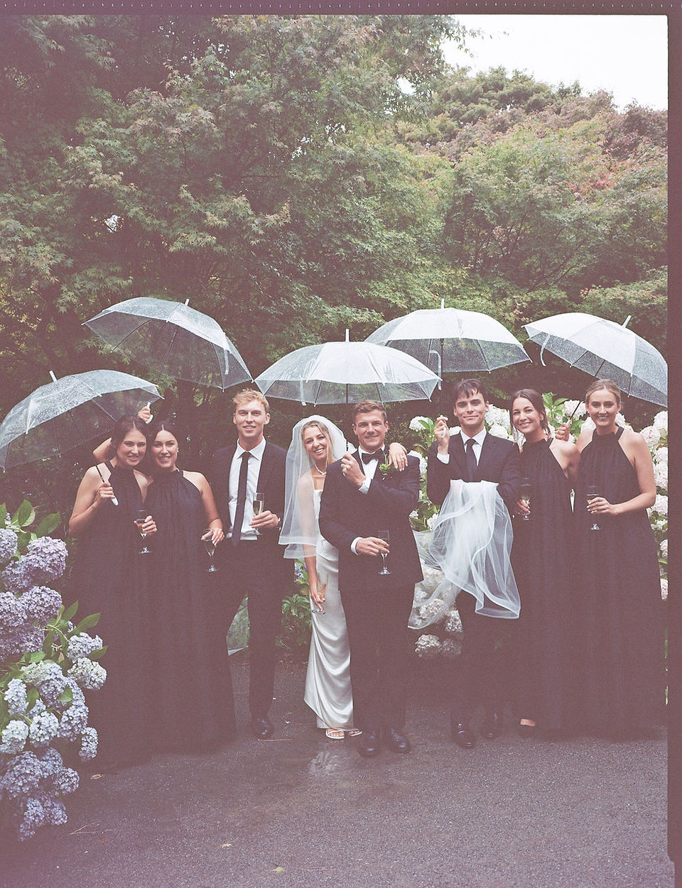 Vintage-style photo of the wedding party posing under umbrellas in the garden