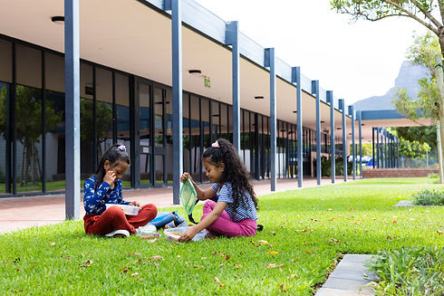 Two biracial girls are eating lunch on a school lawn Dressed in casual clothes, they enjoy