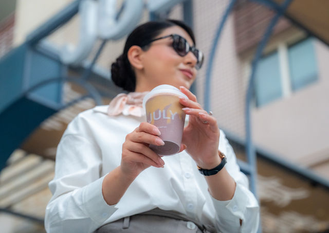 Woman holding coffee cup, wearing sunglasses, outdoors.