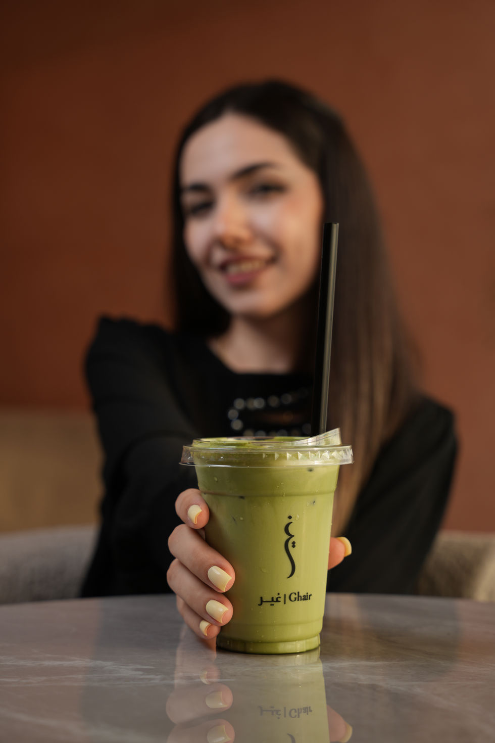 Woman holding iced pistachio matcha drink from Ghair Café