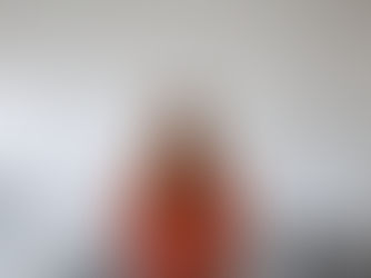 A person in a red sweater stands in an art gallery with white sculptural figures, some suspended, creating a dynamic and creative atmosphere.